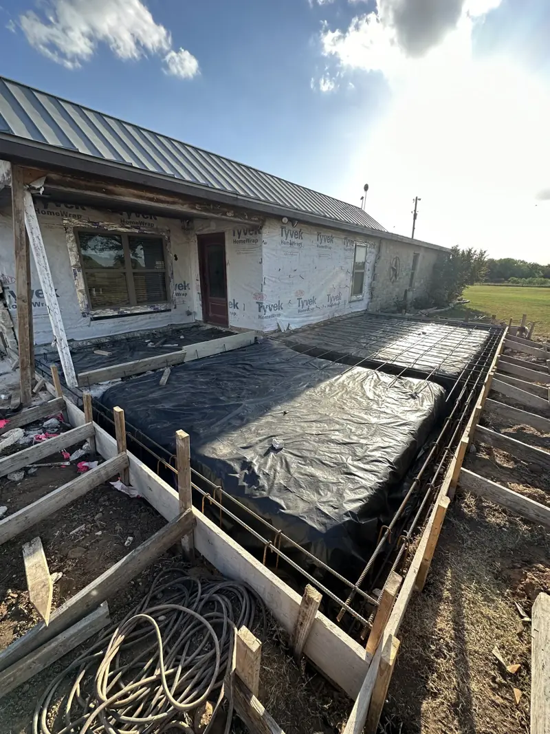 Forms, rebar and black plastic set for an addition slab along a house in house wrap.