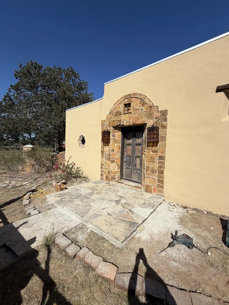 New flagstone porch in front of an arched stone entry with a wooden double door on a stucco house.