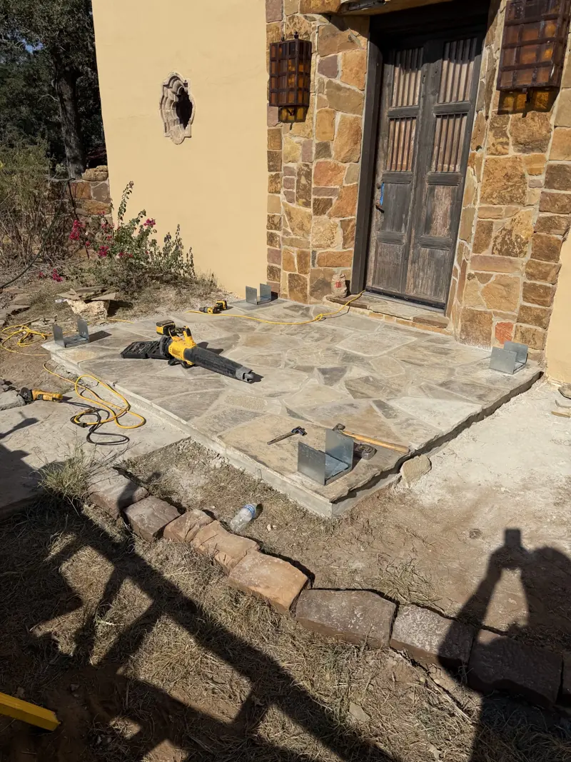Steel post bases set on the corners of the flagstone porch, with tools lying on the stone.