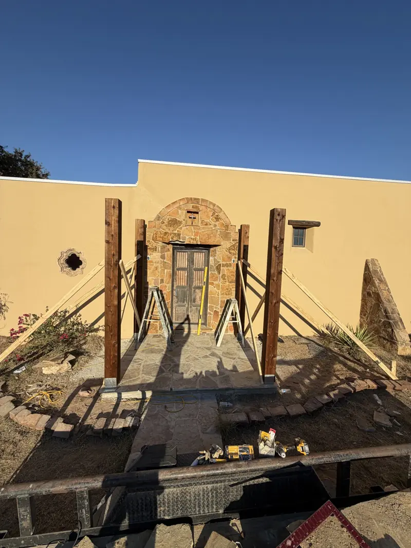 Front view of the stone entry with four braced cedar posts on the porch and ladders by the door.