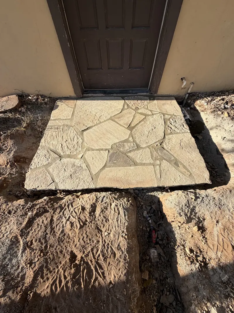 New flagstone landing at a brown paneled door in a stucco wall.