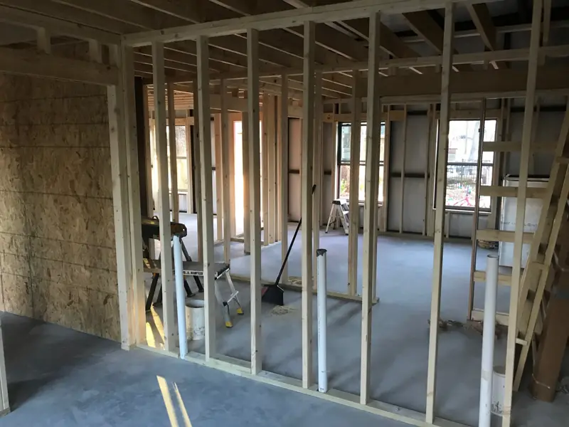 Interior walls framed in wood, with sheathing on one wall and pipes coming up through the slab.