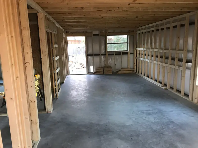 Framed walls and ceiling joists finished, looking toward a door and window.