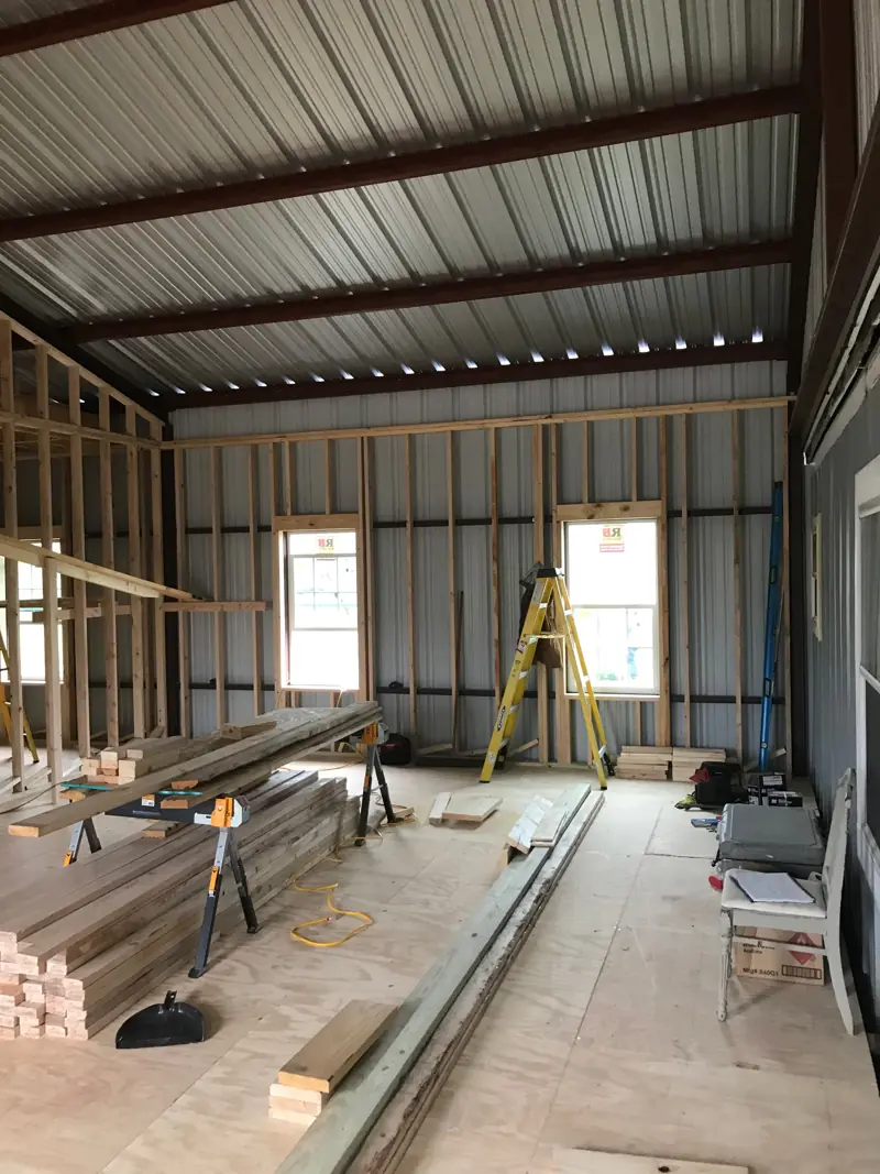 Plywood floor, lumber and sawhorses inside the steel building, windows along the wall.