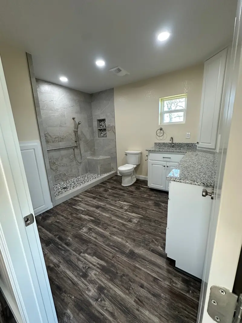 Bathroom with a gray tile walk-in shower, a bench and niche, a vanity with a speckled stone top and wood-look plank floors.