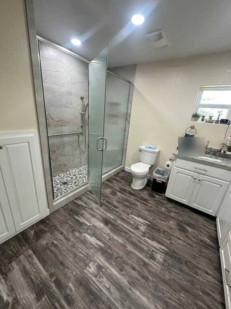 Textured glass shower doors open on the tiled walk-in shower, beside the toilet and the vanity.