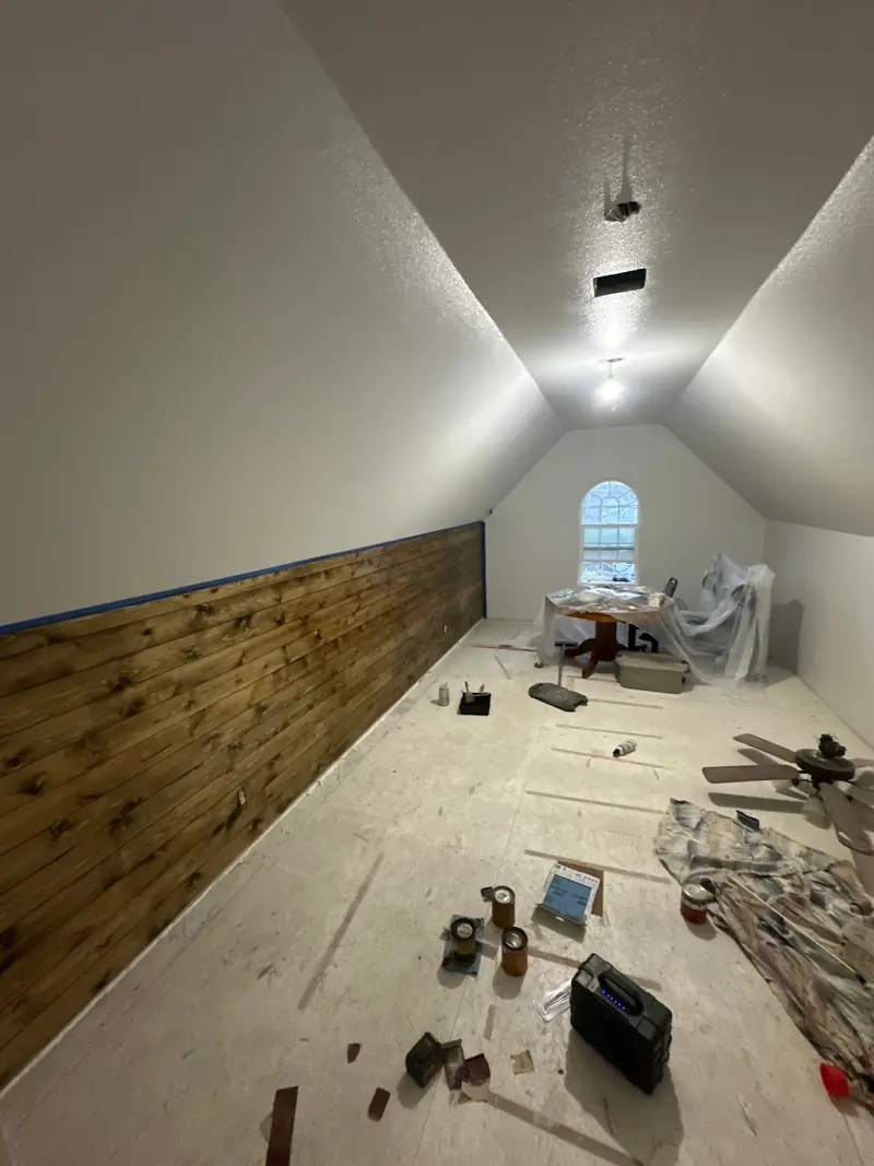 Upstairs bonus room under a sloped ceiling, with a stained wood plank wall up and the floor still bare.