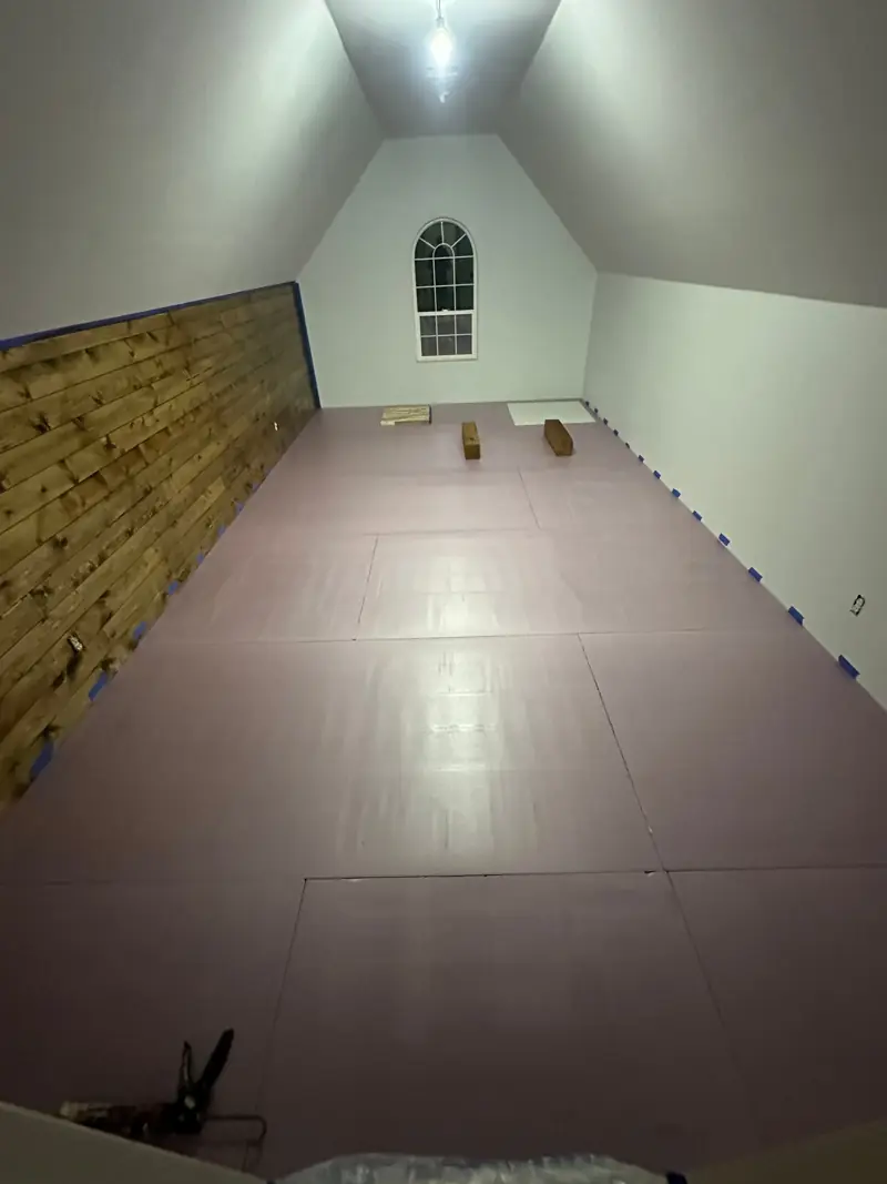 The bonus room floor covered in pink panels before the new flooring, below an arched window.