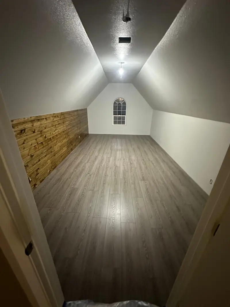 New gray plank flooring down the length of the bonus room, beside the stained wood wall.