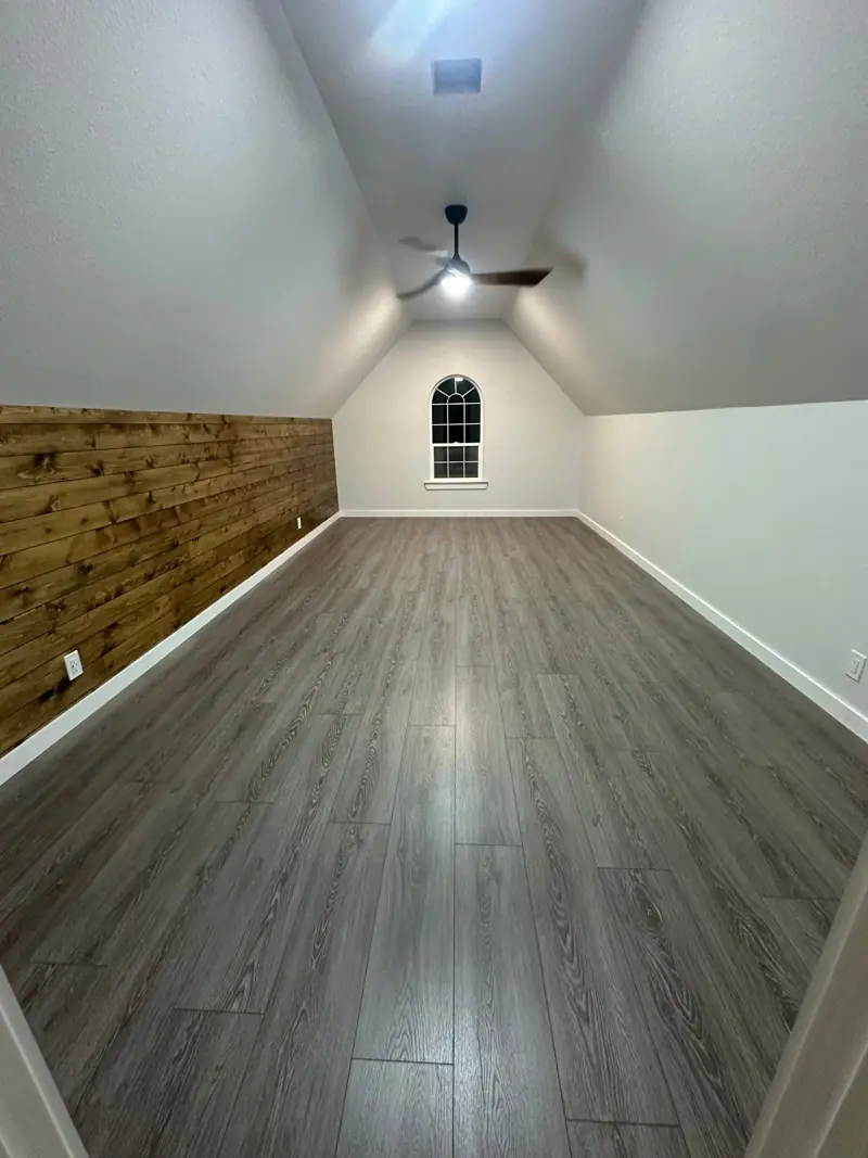 The finished bonus room with gray plank floors, the stained wood wall and a ceiling fan.