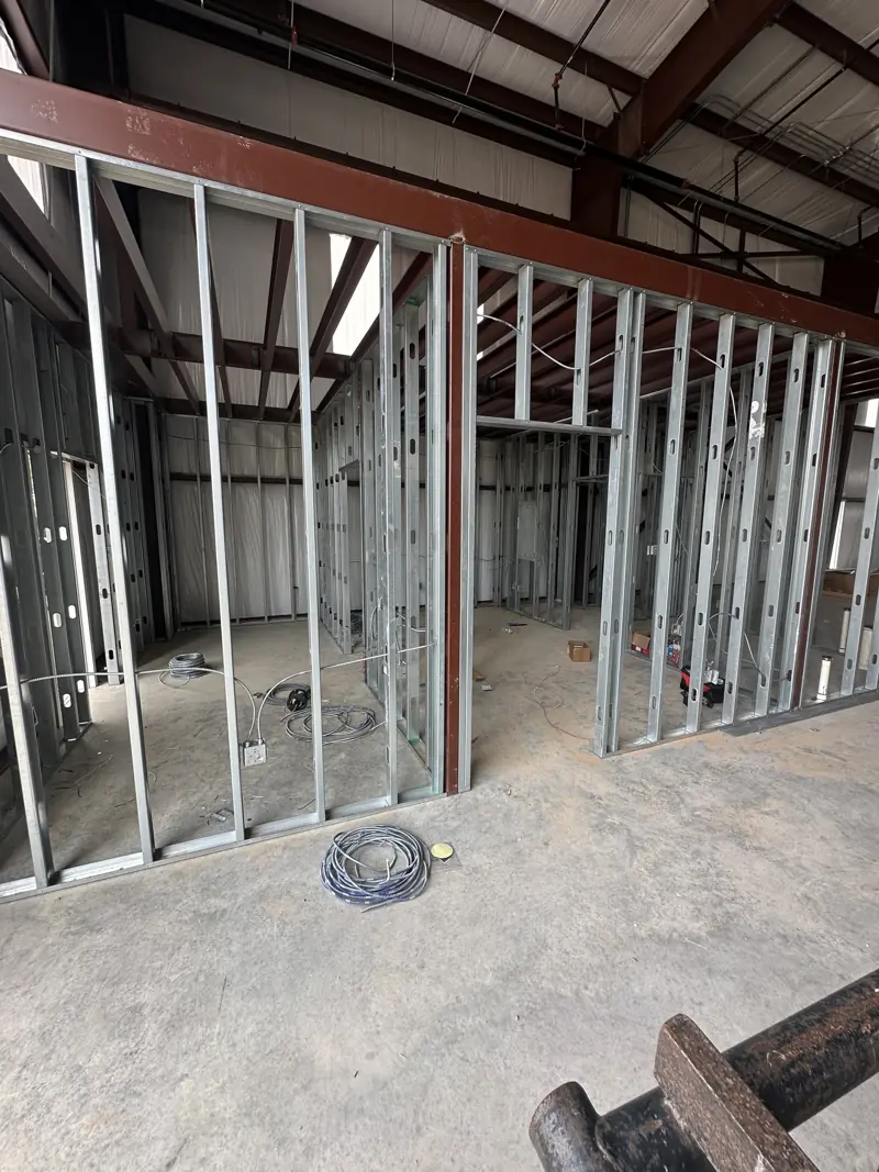 Metal stud partition walls with door openings and coiled metal-clad electrical cable on a concrete floor.