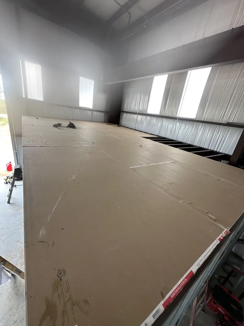 Fire-rated gypsum board laid across the steel mezzanine framing, with part of the joists still open.