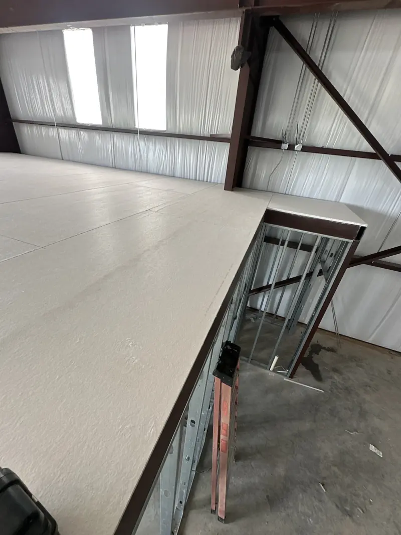 Light gray board decking covering the mezzanine top, with steel edge trim and metal stud framing below.