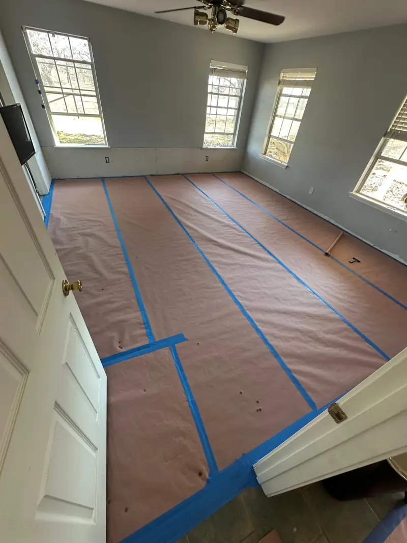 Bedroom with new drywall on the lower walls and the floor covered in brown paper and blue tape, ready for paint.
