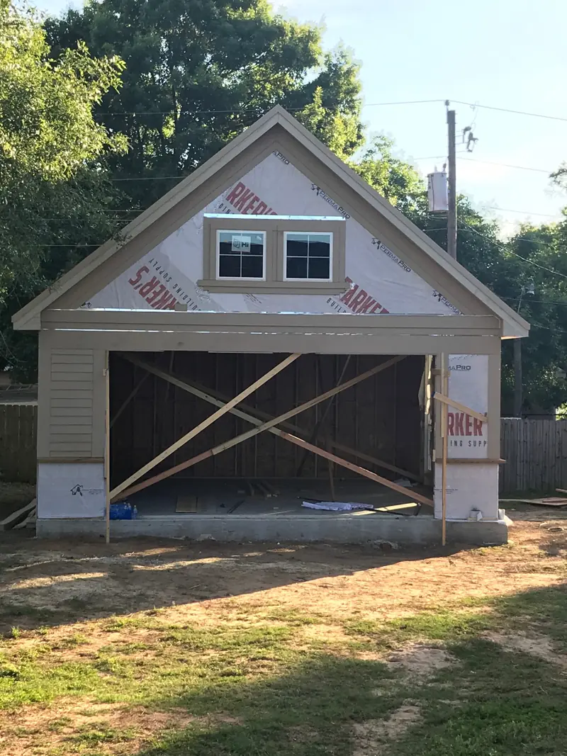 Front of the garage in house wrap, with two windows in the gable and a braced door opening.