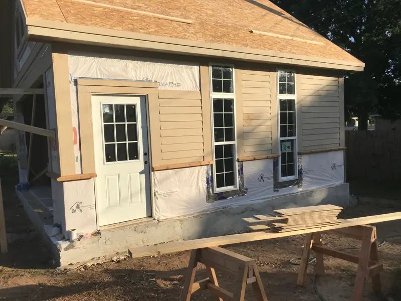 Side of the garage with a door, tall windows and lap siding going on over the wrap.
