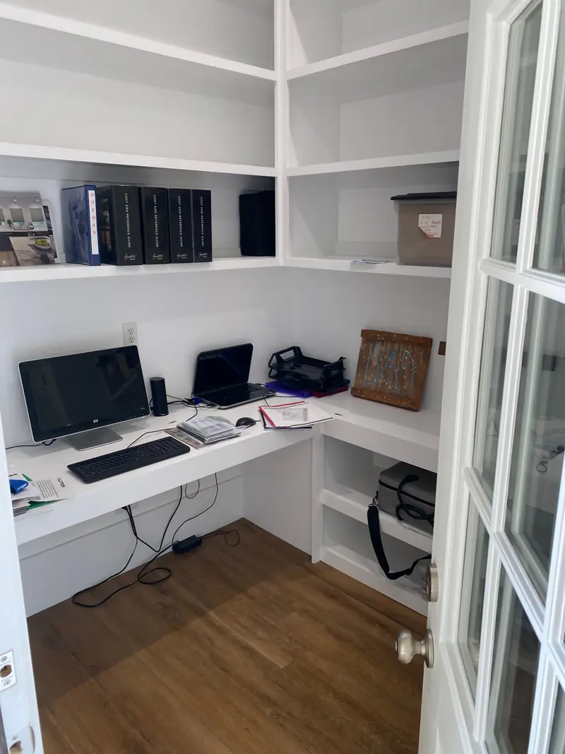 Home office with white built-in shelves, a corner desk and French doors.