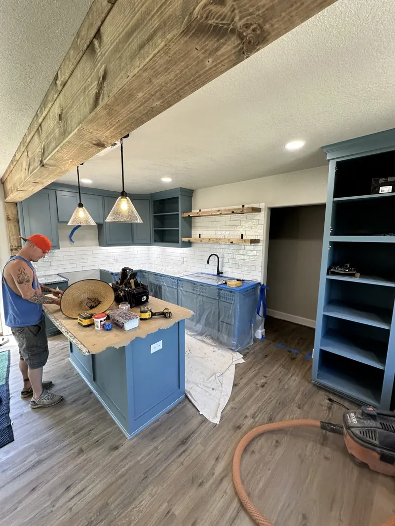 Kitchen with blue cabinets, an island, white subway tile, pendant lights and a wood beam overhead.