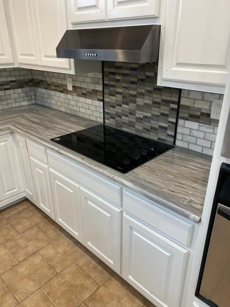Kitchen with painted white cabinets, new counters and a glass mosaic backsplash.