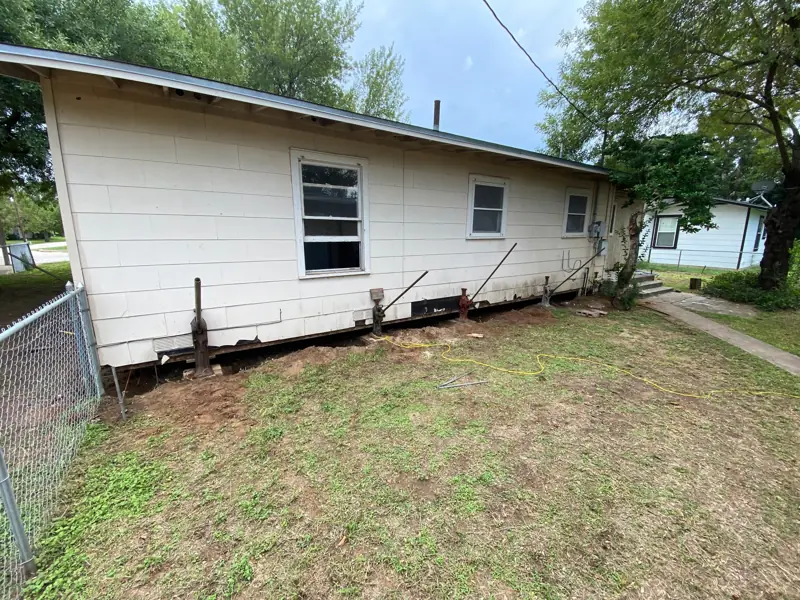 Pier-and-beam house with the skirting off and jacks set along the side.