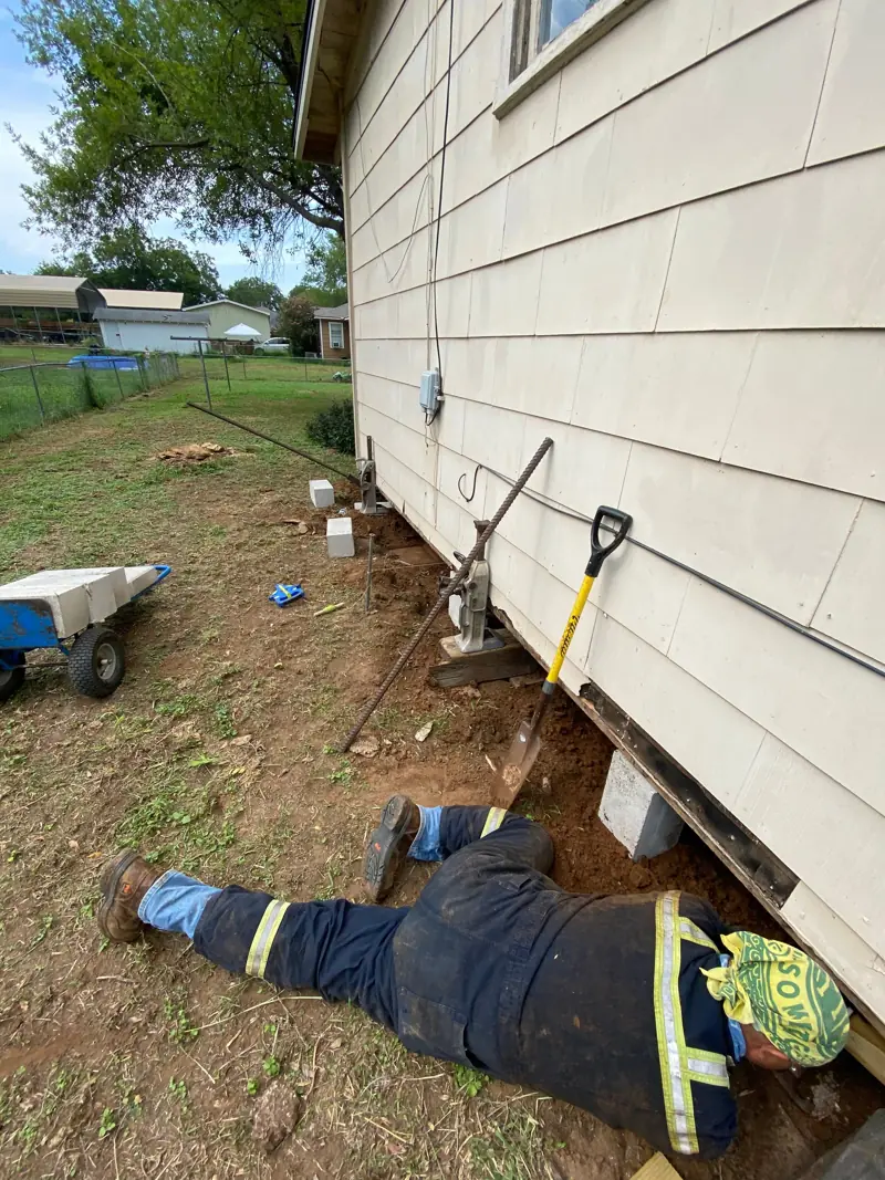 Crew member under the house setting a jack on blocks.