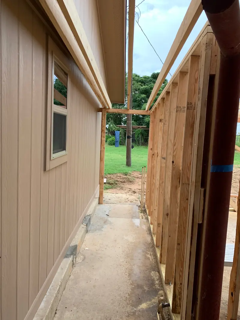 New wall framed beside the existing wall of the house under the metal roof.