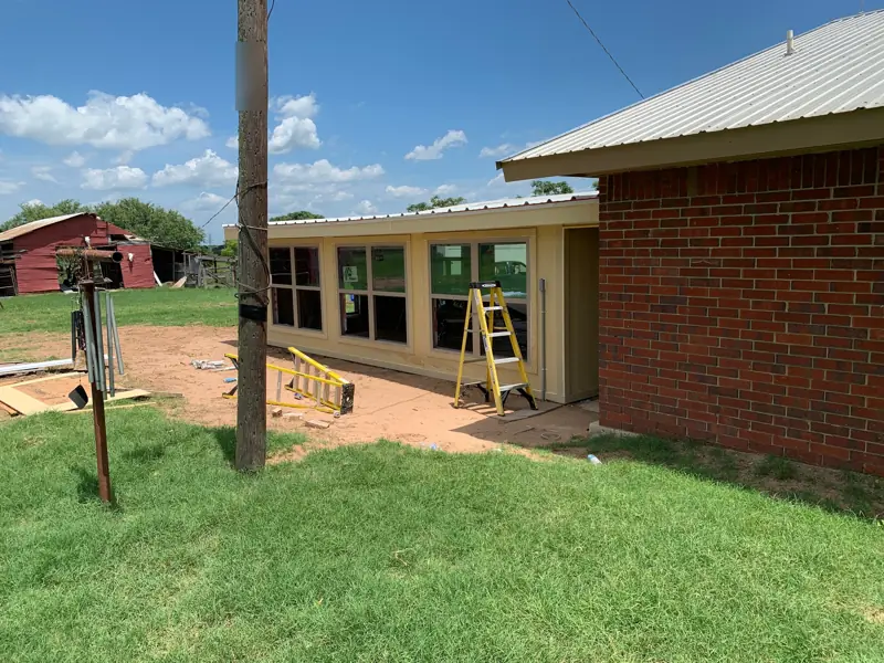 Outside: the closed-in room with a row of windows, beside the brick house.