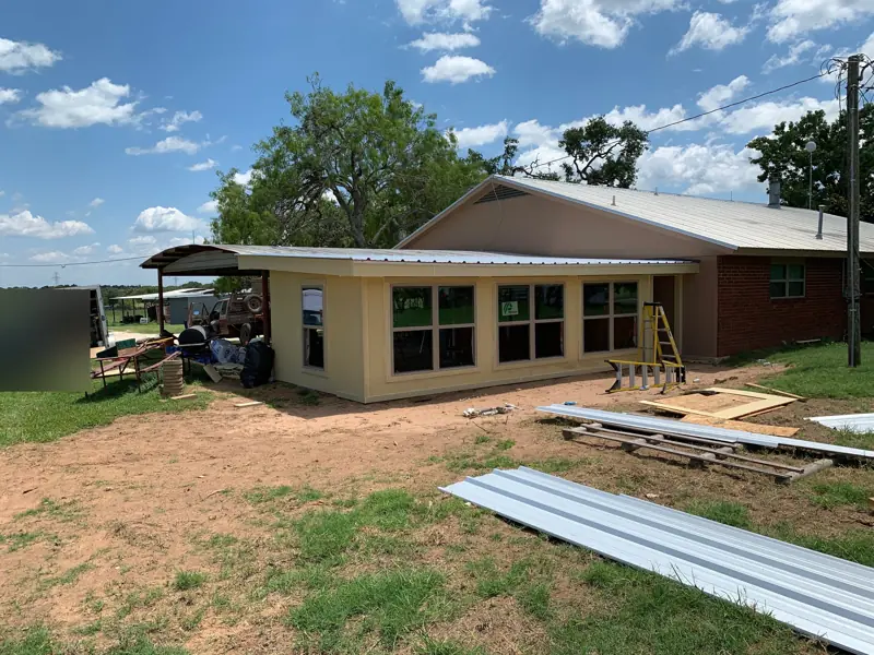 Wider view of the new room with its row of windows, metal roof panels on the ground.