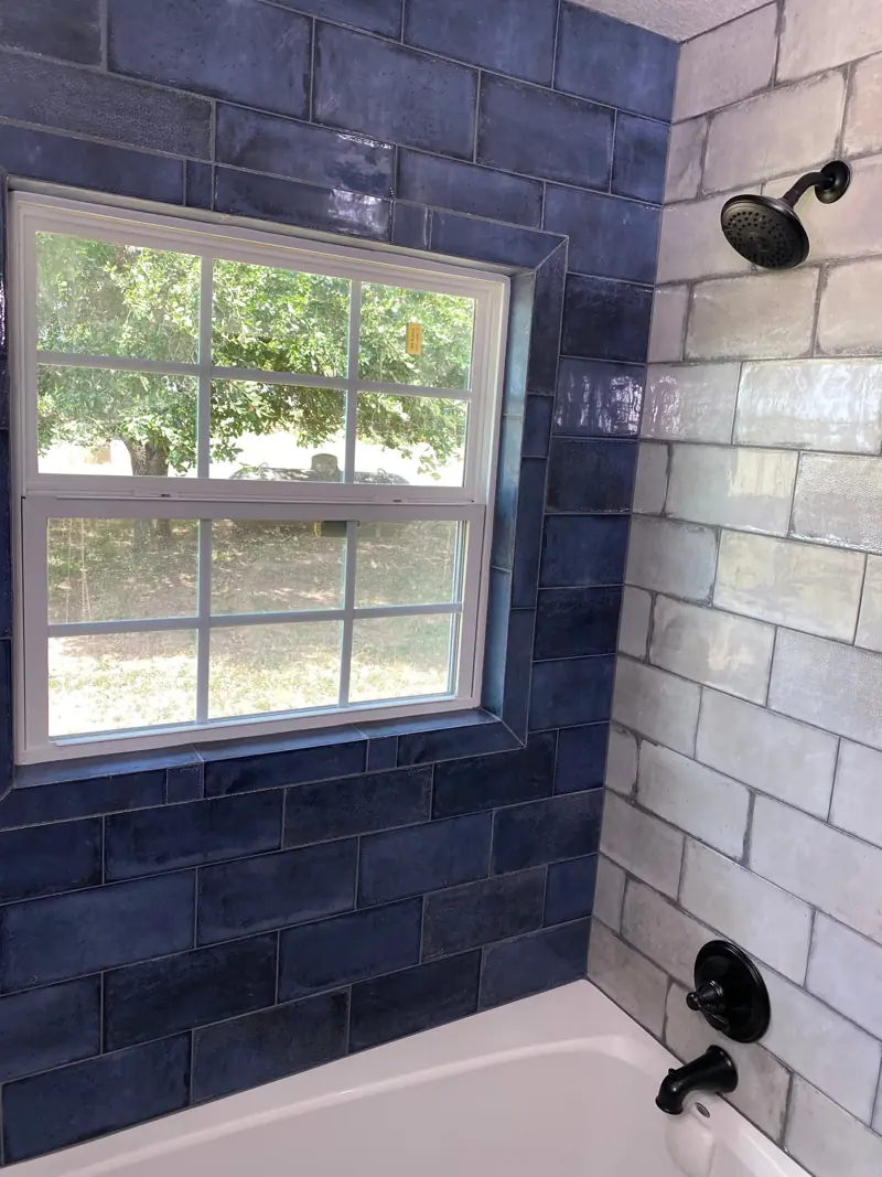 Navy and white tile tub surround around a window, with black fixtures.