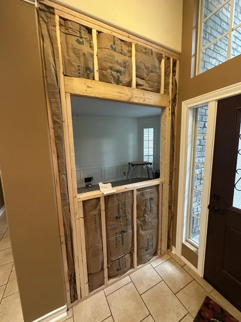 Newly framed stud wall with kraft-faced insulation and a window opening, next to the front door and tile foyer.