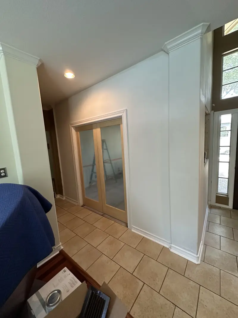 Finished new wall with glass-panel double doors, white trim and crown molding, seen from the tiled hallway.