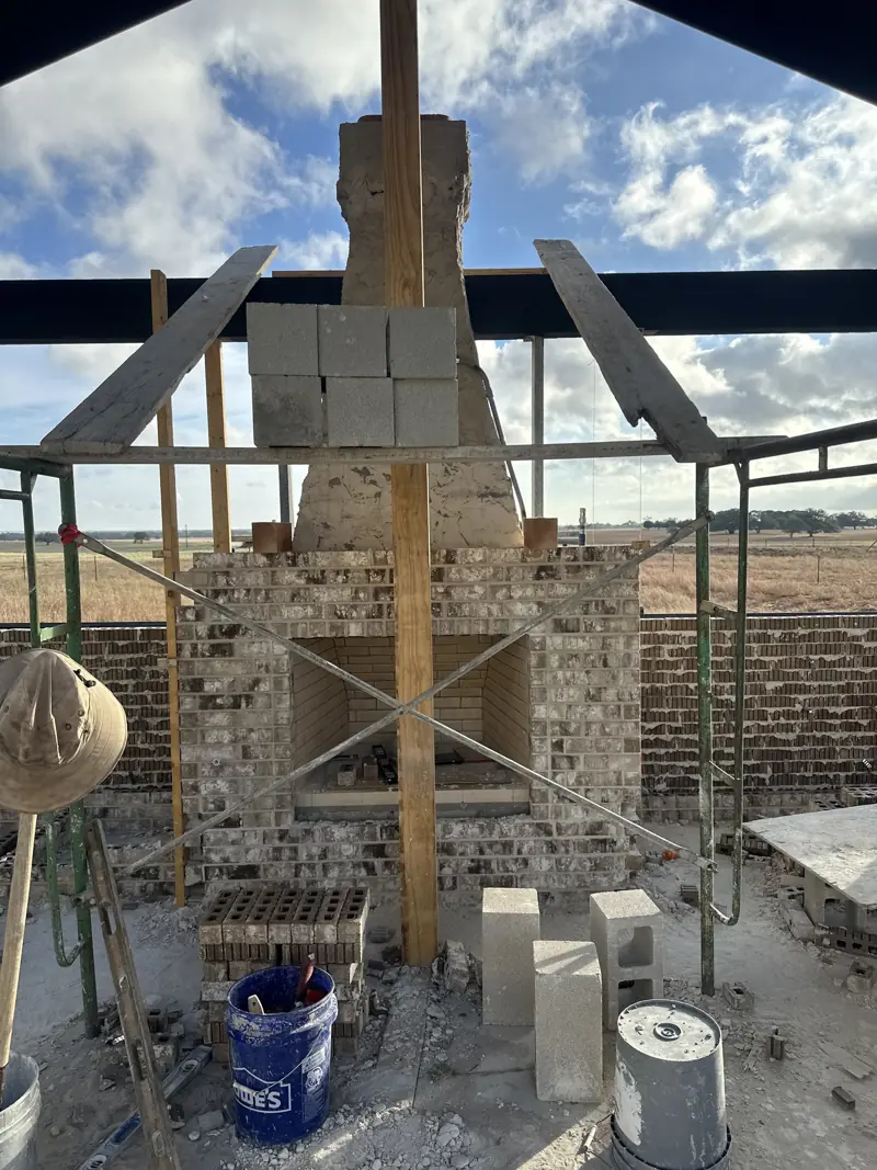 Brick fireplace face with a firebrick-lined firebox and mortar-coated chimney, surrounded by scaffolding and block.