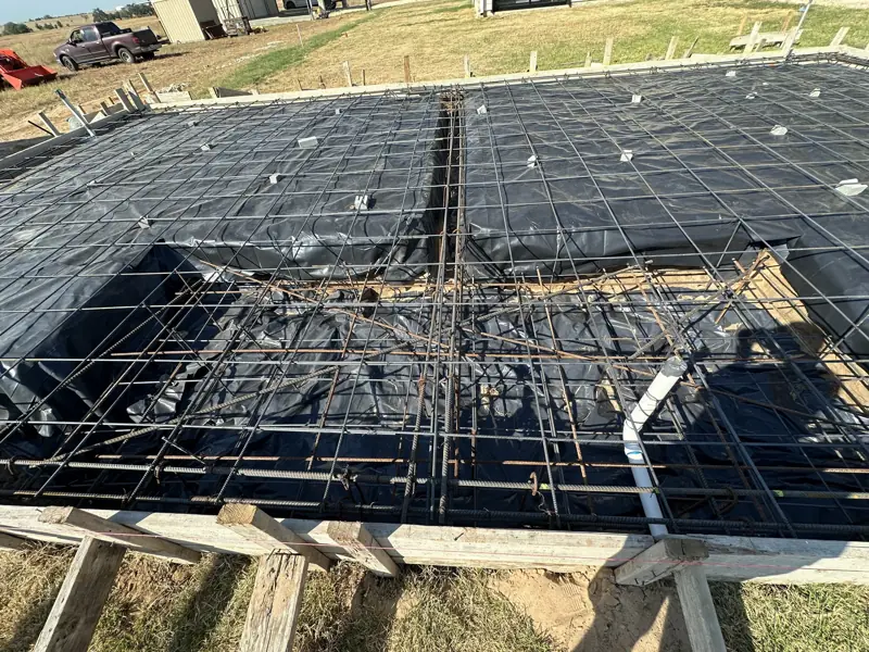 Rebar mat and form boards over black plastic, ready for a concrete slab in an open field.