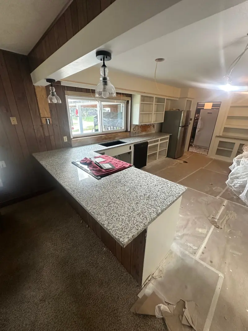 Kitchen with the cabinets freshly painted white, new granite on the peninsula and under the window, and glass pendant lights.