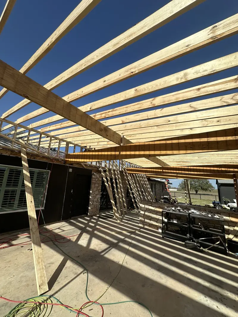 New wood rafters and beams framed over the patio, seen from below against a clear blue sky.