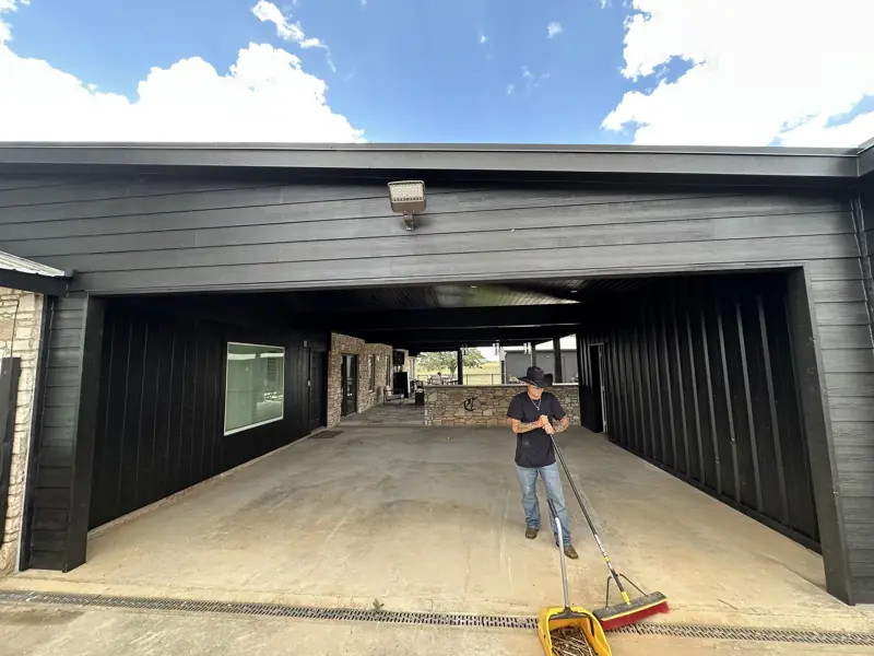 Finished breezeway with black lap siding, new fascia and floodlight, a worker sweeping the concrete slab.