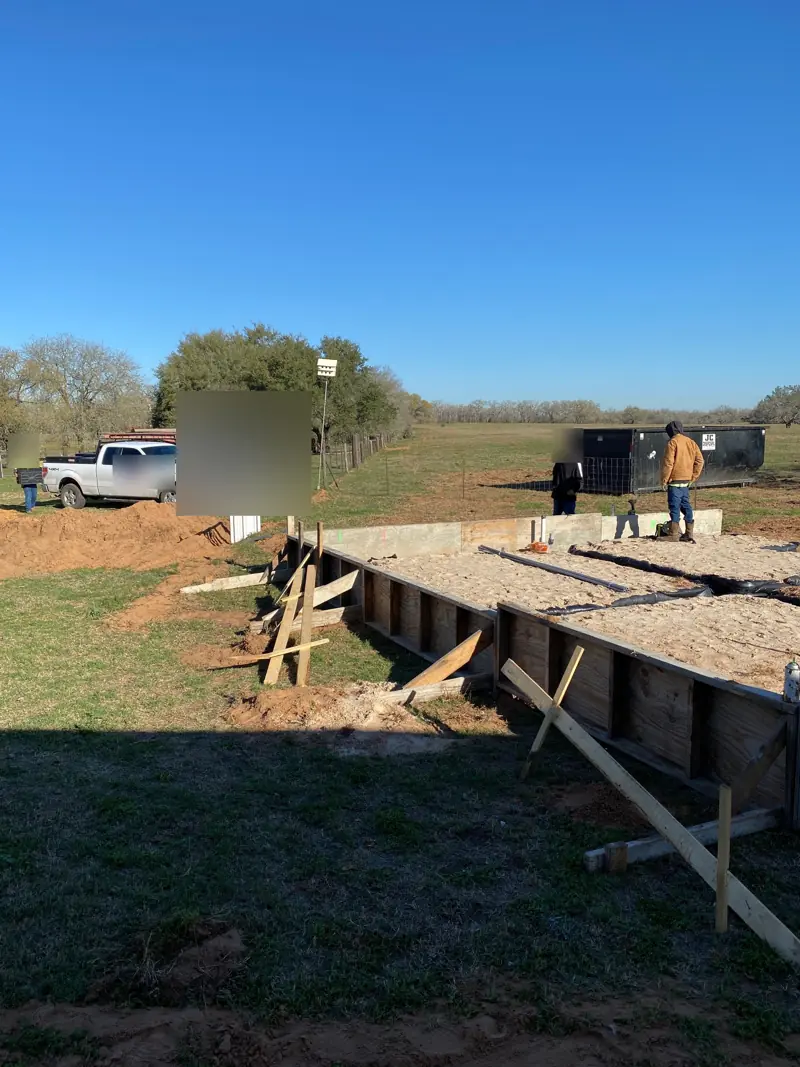 Wood forms over a gravel base for a slab on open pasture, trucks parked beyond.
