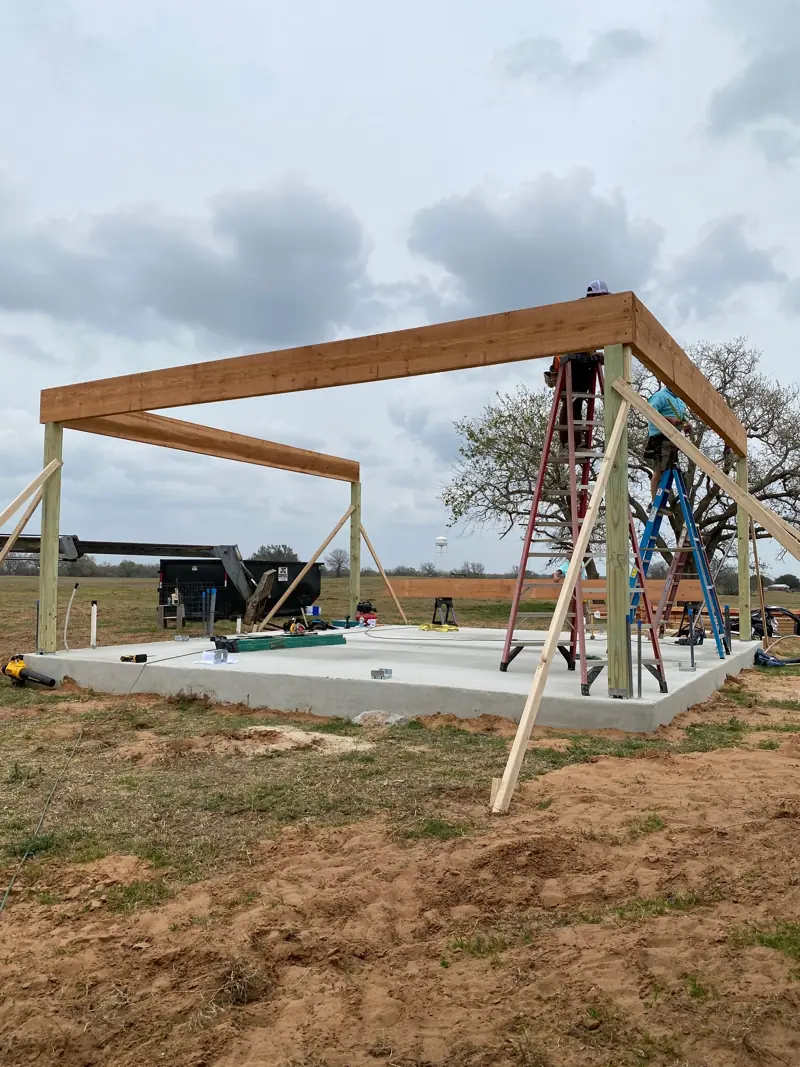 Cedar posts and beams standing on the slab, braced, with crew on ladders.