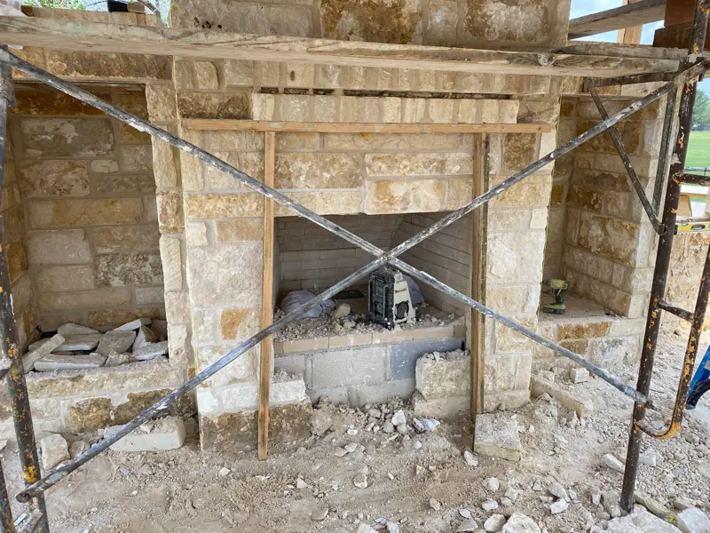 Stone outdoor kitchen base going up behind scaffolding.
