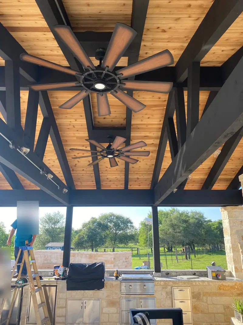 Finished cedar ceiling with black beams and ceiling fans over the outdoor kitchen and grill.