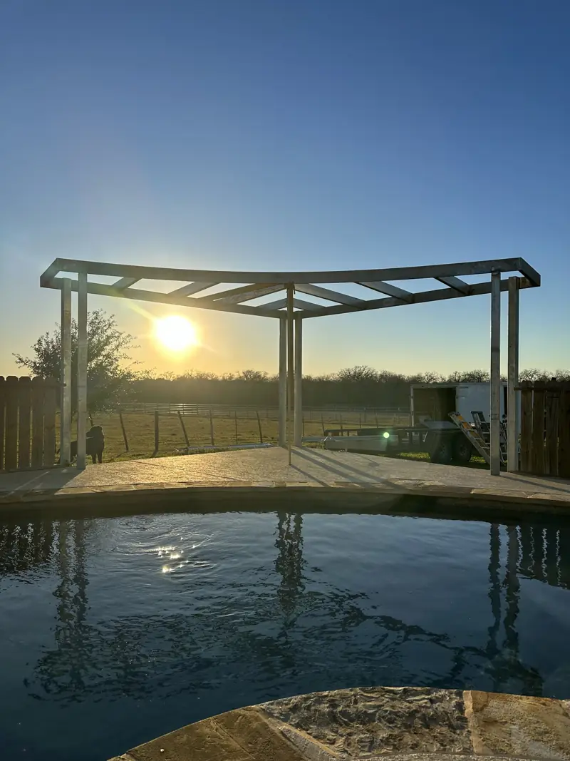 Rounded steel frame for a pool cover rising beside a pool at sunset.