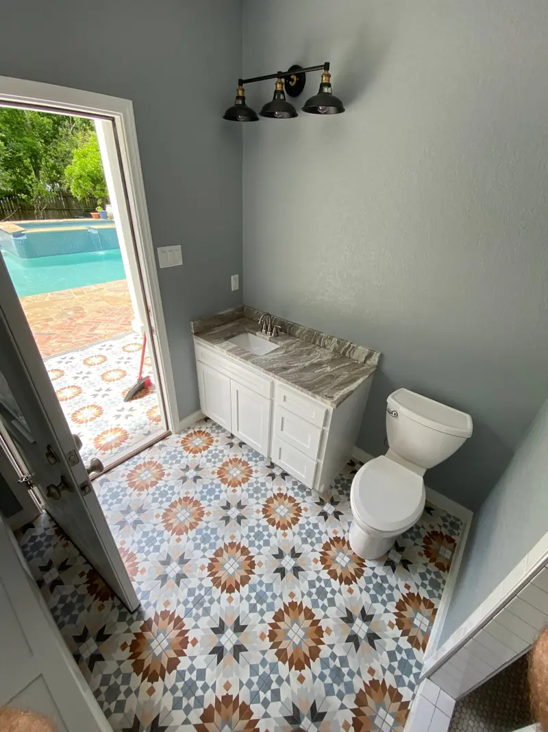 Pool house bathroom with a patterned tile floor, a white vanity and black sconces.