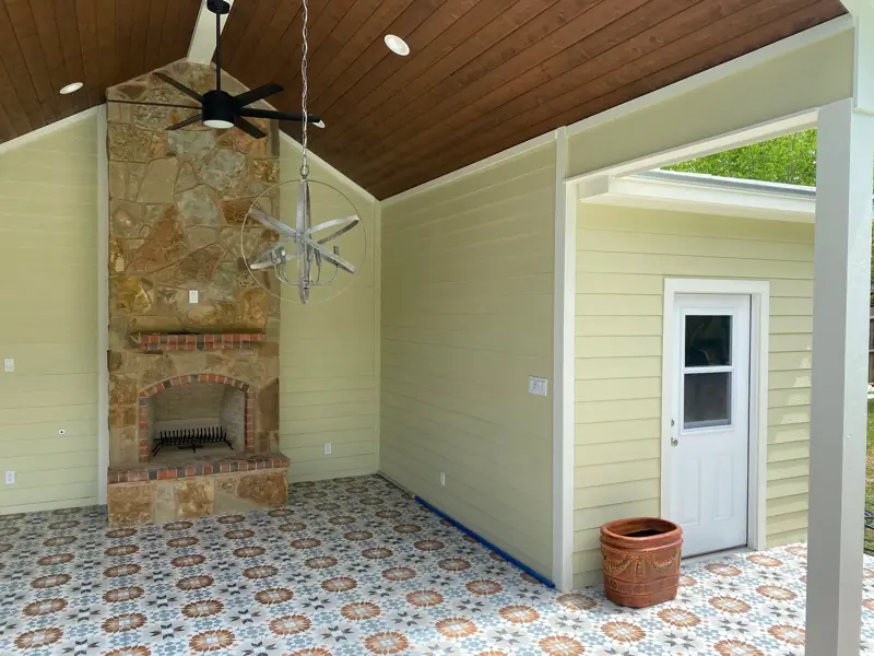 Stone fireplace with brick accents under the wood ceiling, a fan above and a door to a room.