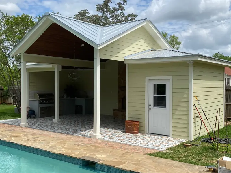 Pool house from across the pool: wood ceiling under the gable, lap siding and a metal roof.