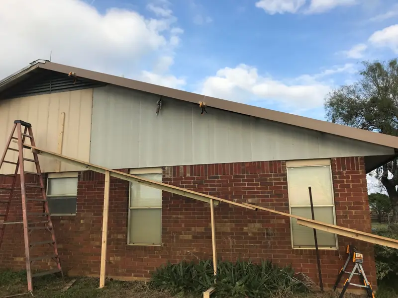 Brick ranch house with new siding going on the gable above the brick, ladders and boards against the wall.