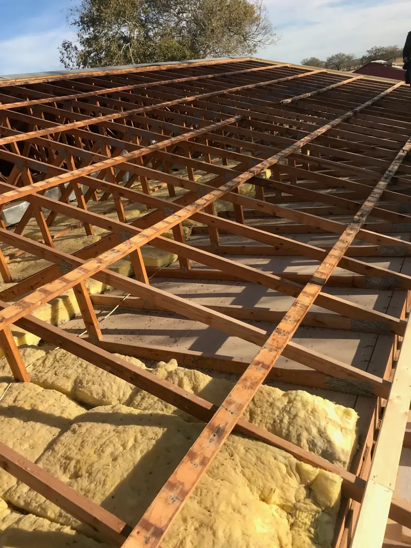 Roof stripped to the rafters and old boards, with insulation showing between them.