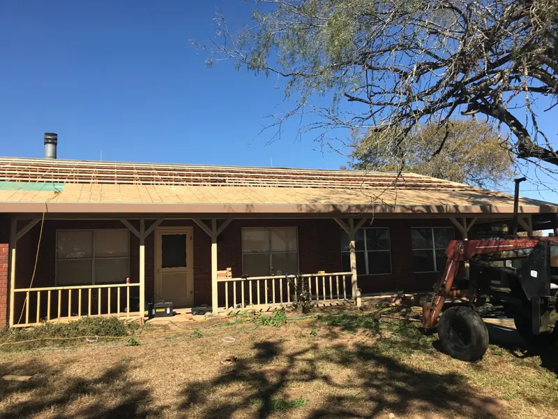 New roof decking across the whole front slope, a tractor parked beside the porch.