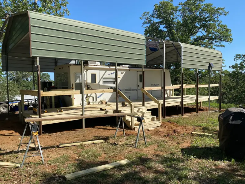 Finished deck with stairs and railing under the green metal RV cover.