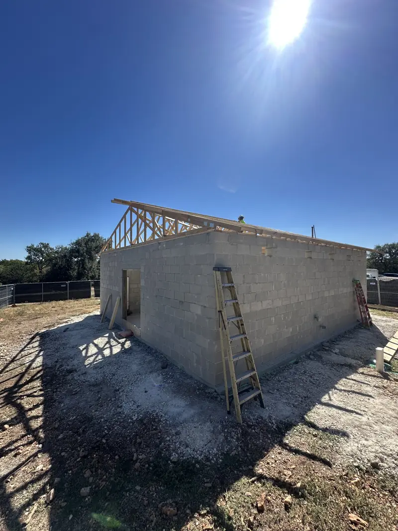 Wood roof trusses being set on a concrete block building, with ladders against the walls in bright sun.