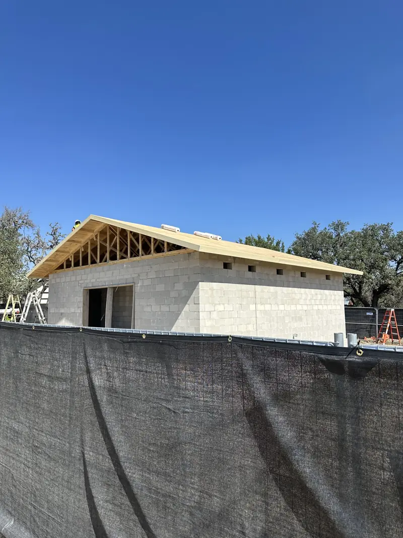 Wood roof decking over trusses on the block building, with underlayment rolls on top and a fence in front.